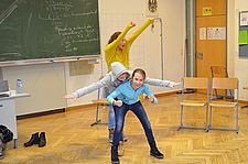 Foto von drei lachenden Schülerinnen in der Klasse, die hintereinander stehen und die Arme ausgestrecken